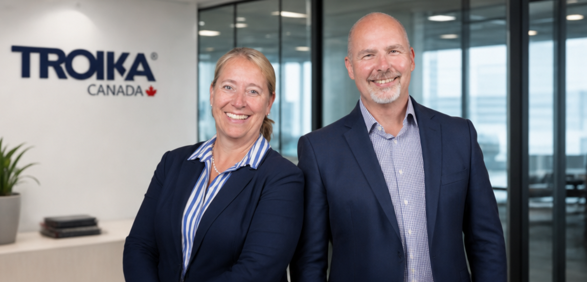 Two professionals standing in an office setting with Troika Canada logo in the background